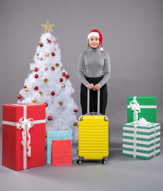 Donna che indossa il cappello di Babbo Natale con i bagagli accanto all'albero di Natale