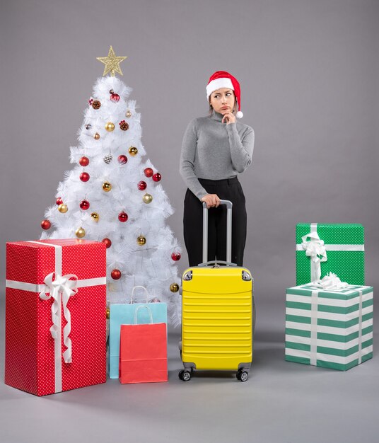 Donna che indossa il cappello di Babbo Natale con i bagagli accanto all'albero di Natale