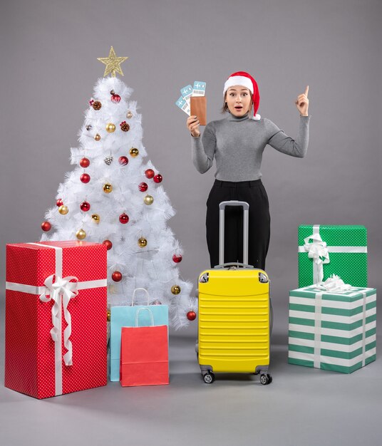 Donna che indossa il cappello di Babbo Natale con i bagagli accanto all'albero di Natale