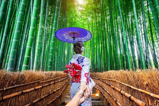Donna che indossa il kimono tradizionale giapponese che tiene la mano dell'uomo e lo conduce alla foresta di bambù a Kyoto, Giappone.