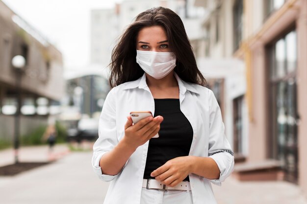 Donna che indossa la maschera mentre va al lavoro mentre guarda lo smartphone