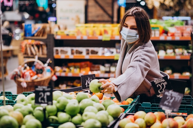 Donna che indossa la maschera per il viso e lo shopping nel negozio di alimentari