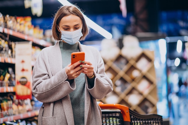 Donna che indossa la maschera per il viso e lo shopping nel negozio di alimentari