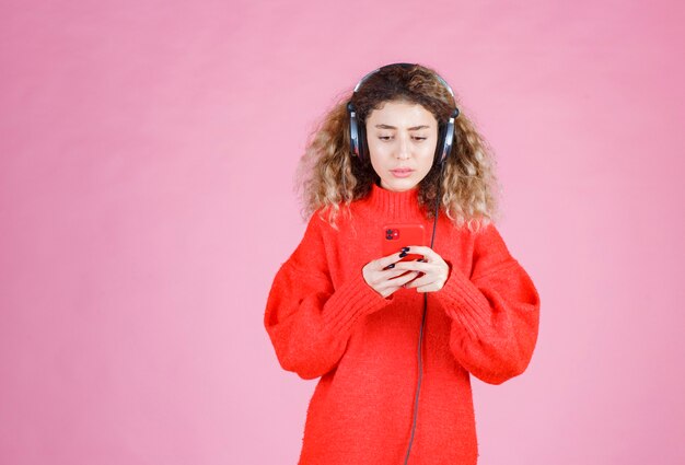 donna che indossa le cuffie che ascolta la sua playlist sullo smartphone e sembra insoddisfatta.