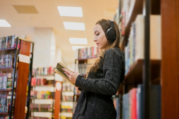 Donna che indossa le cuffie intorno al libro di lettura del collo