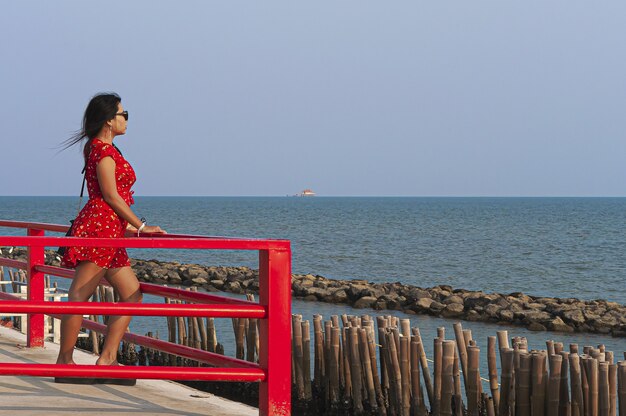 Donna che indossa occhiali da sole e un vestito rosso in piedi sul ponte Red Boardwalk in Thailandia