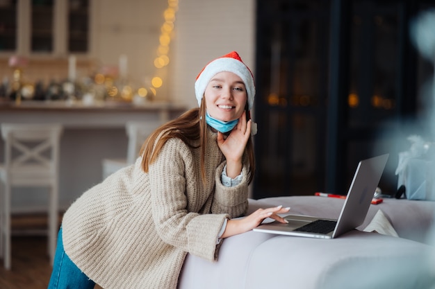 Donna che indossa santa sorridente mentre parla con un amico online sul laptop durante le celebrazioni natalizie a casa