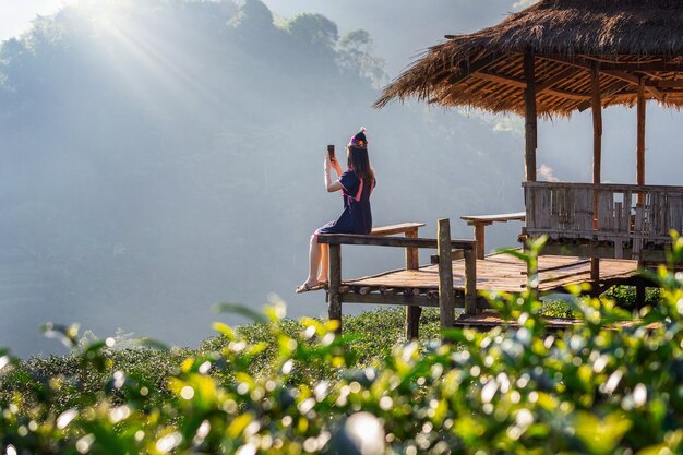 Donna che indossa un abito tribù della collina che si siede sulla capanna nel campo del tè verde.