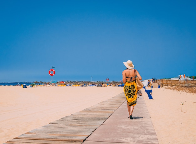 Donna che indossa un bikini e un cappello che cammina sulla spiaggia