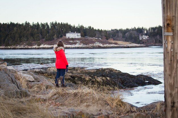 Donna che indossa un cappotto rosso in piedi sulla spiaggia con erba secca di superficie
