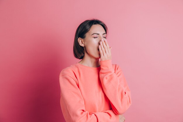 Donna che indossa un maglione casual su sfondo annoiato sbadigliare stanco che copre la bocca con la mano. Irrequieto e sonnolenza