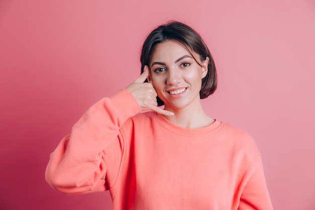 Donna che indossa un maglione casual su sfondo sorridente facendo il gesto del telefono con la mano e le dita come parlare al telefono