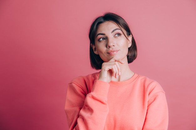 Donna che indossa un maglione casual sulla mano di sfondo sul mento pensando alla domanda, espressione pensierosa. Sorridendo con una faccia pensierosa