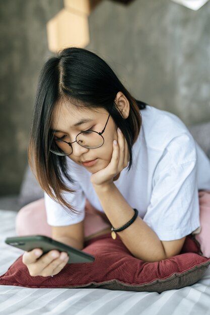 Donna che indossa una camicia bianca sdraiata sul letto e giocando smartphone.
