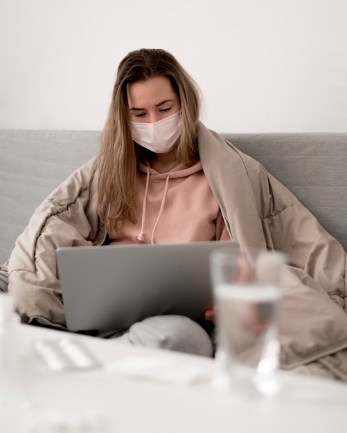 Donna che indossa una maschera medica usando il suo computer portatile