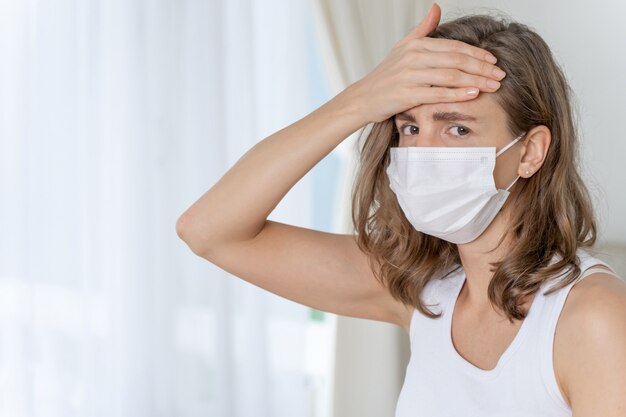 donna che indossa una maschera per proteggere la sensazione di mal di testa e tosse a causa del Coronavirus covid-19 nella stanza di quarantena