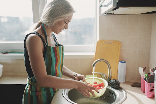 Donna che lava i pomodori degli ortaggi freschi in cucina sotto il flusso dell'acqua