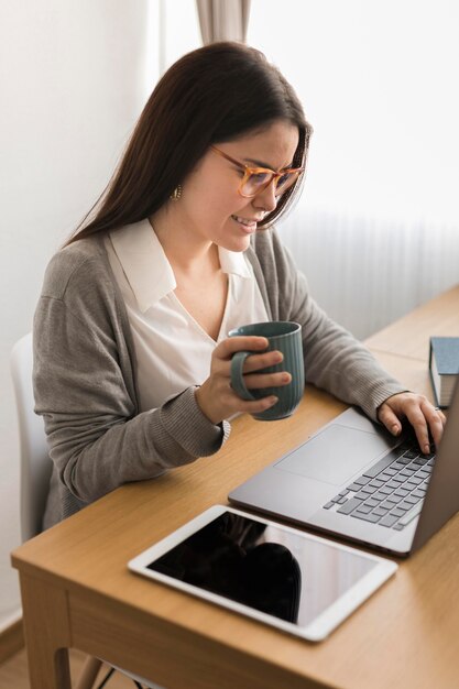 Donna che lavora a casa sul computer portatile e che beve caffè