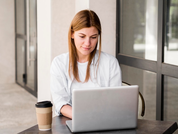 Donna che lavora al computer portatile all'aperto mentre mangia il caffè