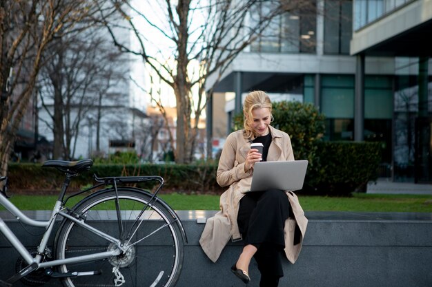 Donna che lavora al suo computer portatile fuori e che beve caffè