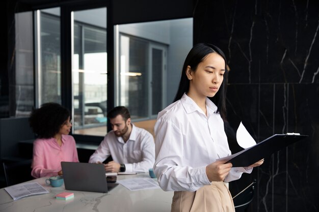 Donna che legge documenti per lavoro mentre i suoi colleghi usano un laptop