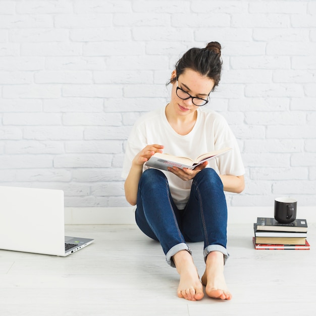 Donna che legge vicino al computer portatile e tazza