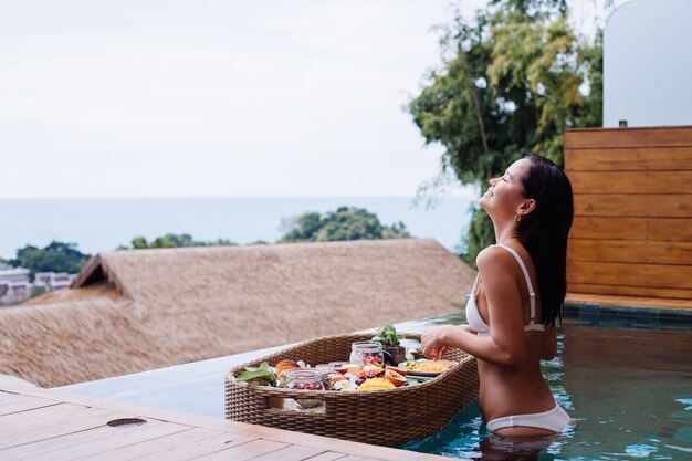 Donna che mangia colazione sana tropicale in villa sul tavolo galleggiante