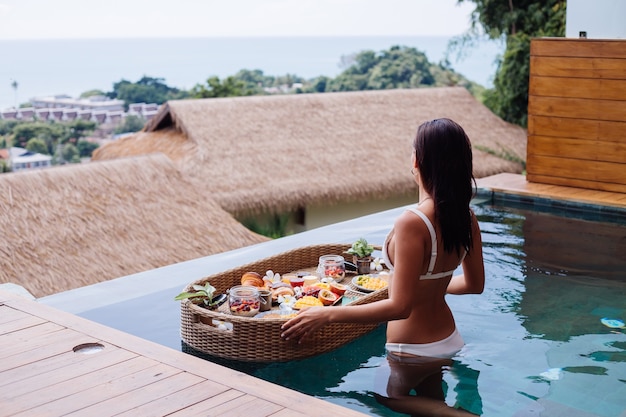 Donna che mangia colazione sana tropicale in villa sul tavolo galleggiante