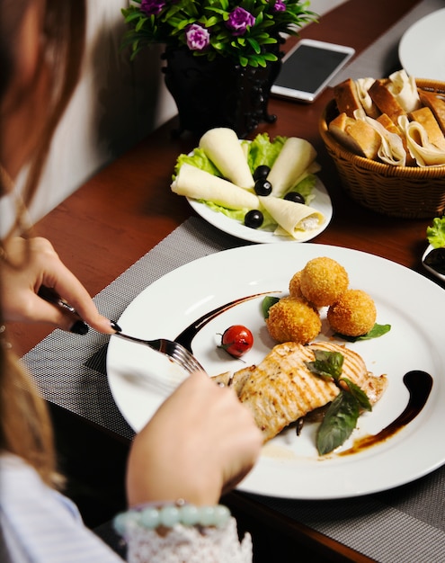 Donna che mangia filetto di salmone al forno con patate e panini al formaggio e verdure mescolate.