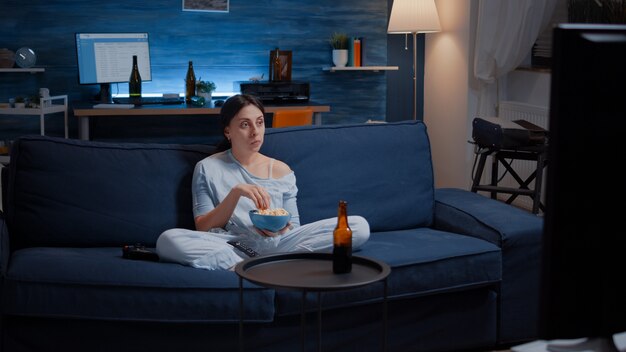 Donna che mangia popcorn e guarda un interessante serial in tv