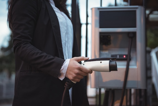 Donna che mantiene caricatore per auto alla stazione di ricarica per veicoli elettrici