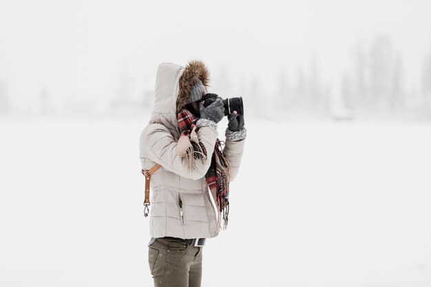 Donna che mette a fuoco con la macchina fotografica nella natura di inverno