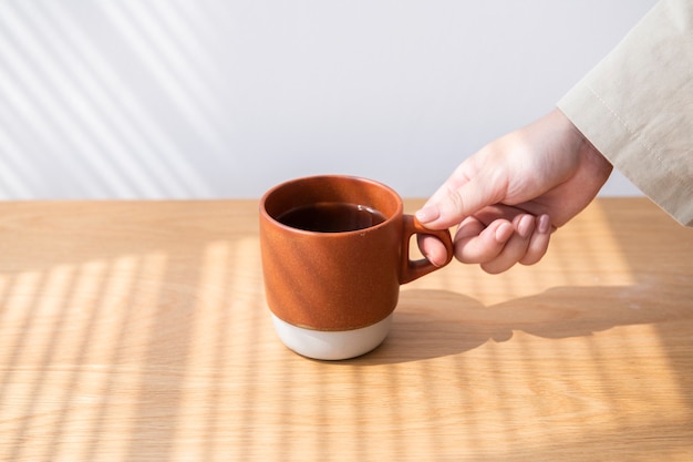 Donna che ottiene una tazza di caffè da un tavolo di legno