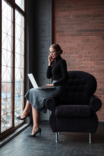 Donna che parla sopra il telefono con il computer portatile