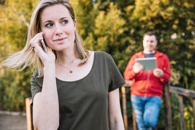 Donna che parla sul telefono vicino uomo sfocato con tavoletta