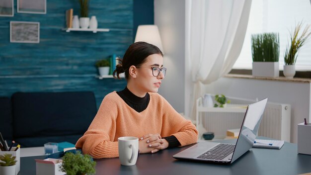 Donna che partecipa a una lezione di videochiamata remota sul laptop, utilizzando la videoconferenza per parlare con l'insegnante durante la lezione scolastica online. Studentessa che ha conversazione in teleconferenza con webcam.