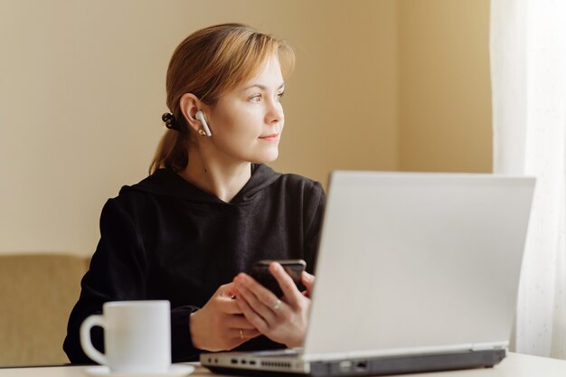 Donna che per mezzo del computer portatile e del telefono cellulare per il suo lavoro a distanza a casa