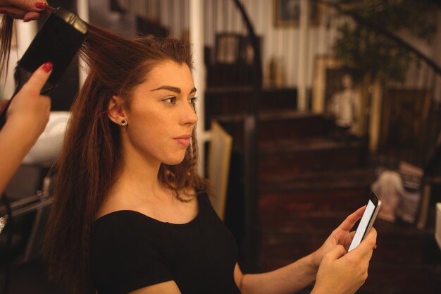 Donna che per mezzo del telefono cellulare mentre raddrizzando i capelli