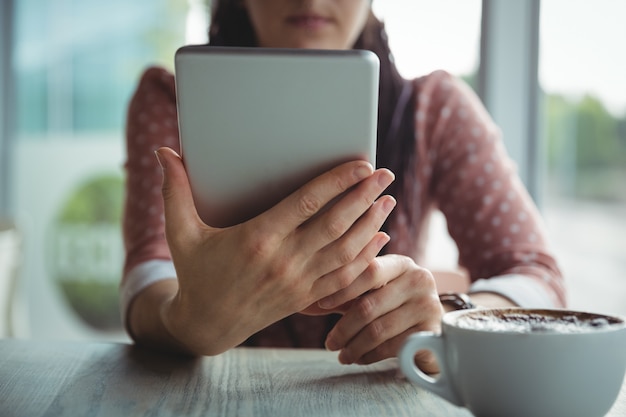 Donna che per mezzo della compressa digitale mentre mangiando tazza di caffè