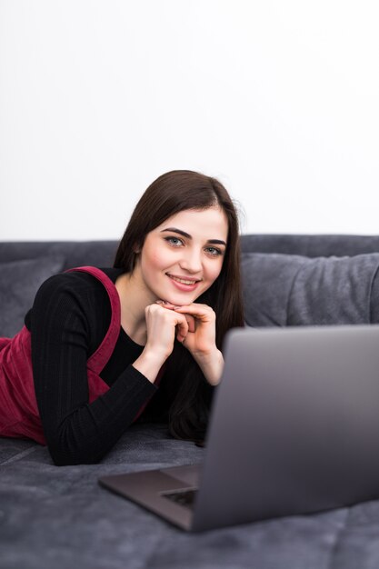 Donna che per mezzo di un computer portatile mentre rilassandosi sullo strato