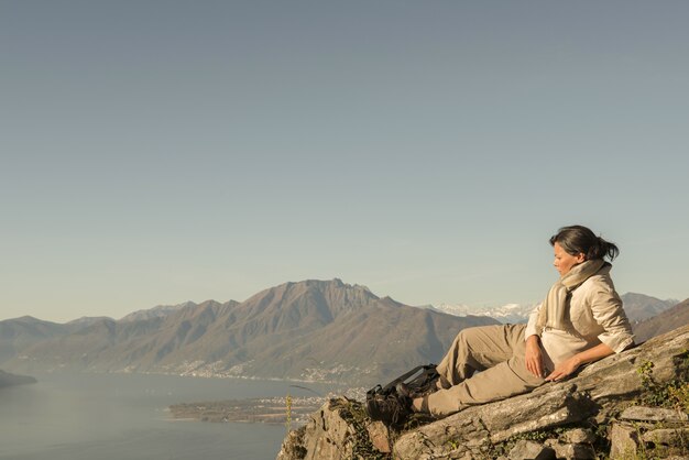 Donna che pone sulla roccia con una bellissima vista di una montagna vicino al mare