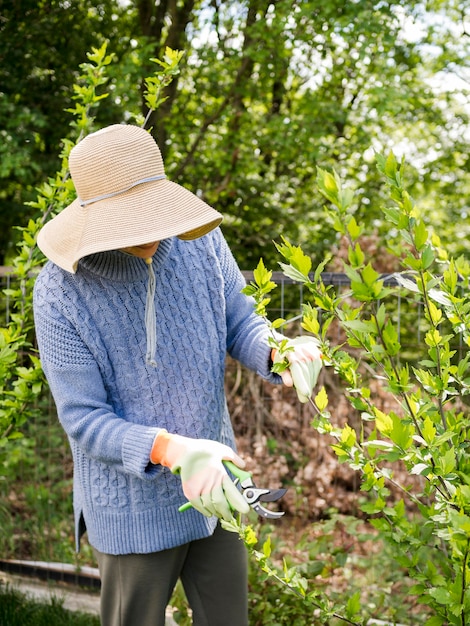 Donna che porta un cappello mentre tagliando le foglie dal suo giardino