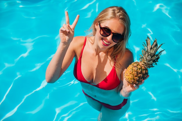 Donna che posa con l&#39;ananas in piscina