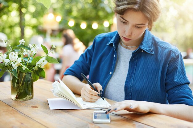 donna che prende appunti utilizzando smartphone. Ritratto all'aperto di una giovane donna che scrive nel suo taccuino