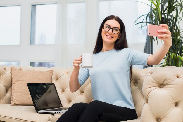 Donna che prende selfie con caffè sul divano