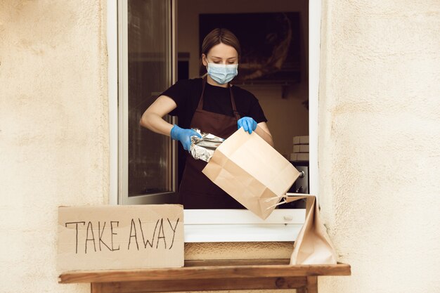 Donna che prepara bevande e pasti, indossando guanti e maschera protettiva.