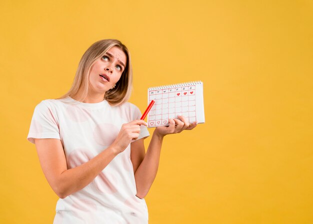 Donna che rotola gli occhi e che mostra il calendario mestruale