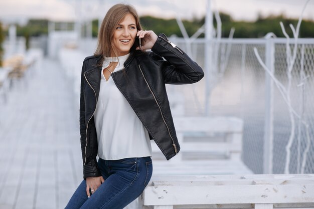 Donna che si appoggia su una tavola di legno bianco parlando al telefono mentre sorridente