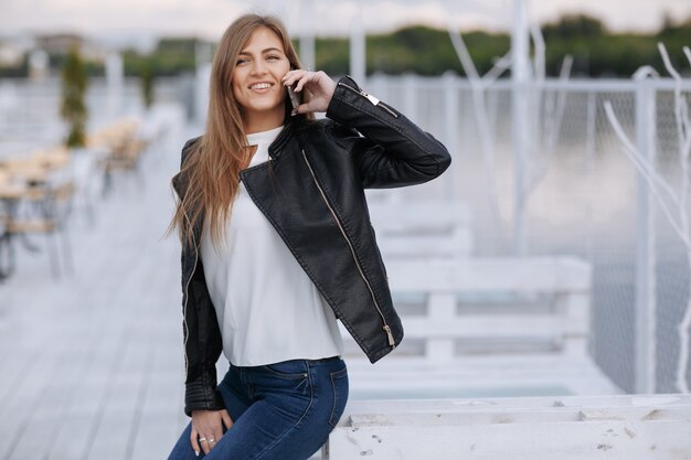 Donna che si appoggia su una tavola di legno bianco parlando al telefono mentre sorridente