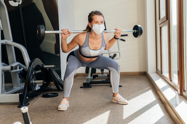 Donna che si esercita in palestra con attrezzature e mascherina medica